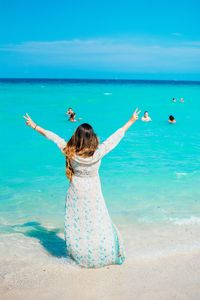 Rear view of woman with arms outstretched showing peace sign at beach