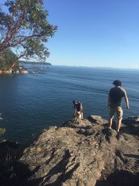 Rear view of men standing on rock by sea against clear sky