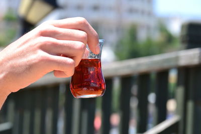 Cropped hand of person holding drink in glass by railing 