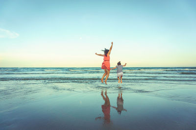 Rear view of woman with daughter jumping at beach