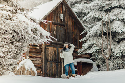 Smiling young woman standing on snow field against cottage