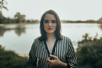 Portrait of young woman standing against lake