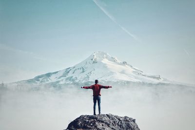 Rear view of person standing on snowcapped mountain against sky