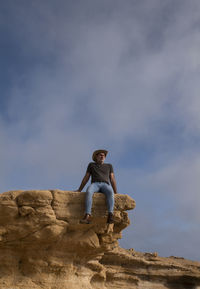 Adult man in cowboy hat sitting on cliff against sky. almeria, spain