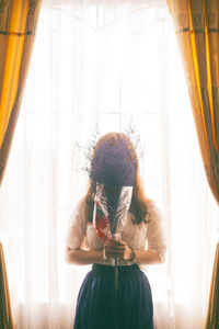 Woman holding bouquet in front of face at home