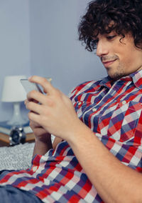 Close-up of man using mobile phone while sitting on bed at home