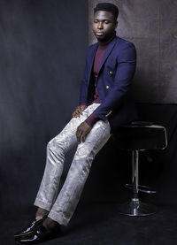 Mid adult man looking away while sitting on chair against wall