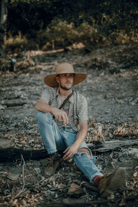 Full length of young man sitting on swing in forest