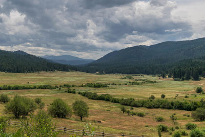 Scenic view of landscape by mountain against cloudy sky