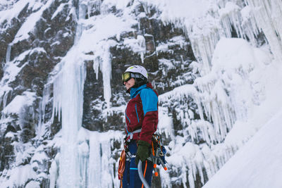 Female ice climber standing at icy cliff