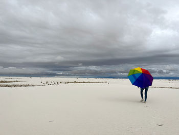 Rear view of man with umbrella on beach against sky
