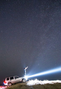 Man standing on car with illuminated headlight against constellation in sky