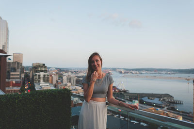 Portrait of young woman standing at building terrace in city