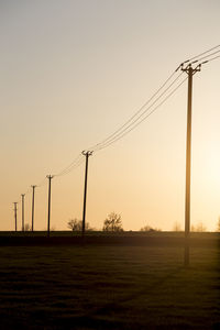 Electricity pylons on field against clear sky during sunset