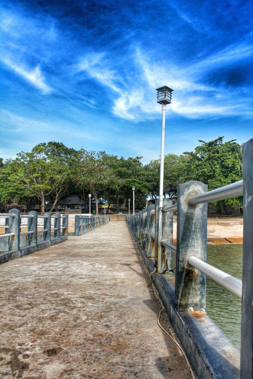 the way forward, sky, street light, railing, tree, cloud - sky, diminishing perspective, vanishing point, lighting equipment, built structure, cloud, transportation, bridge - man made structure, tranquility, nature, connection, footbridge, blue, empty, architecture