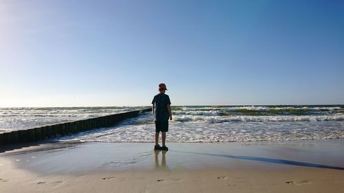 Rear view of boy standing on shore against blue sky