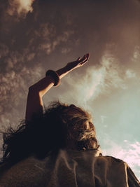 Rear view of man with arms raised against sky during sunset