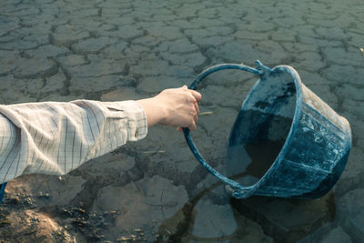 Cropped hand holding bucket on at draught lakeshore