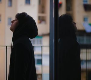 Side view of silhouette woman looking through window at home