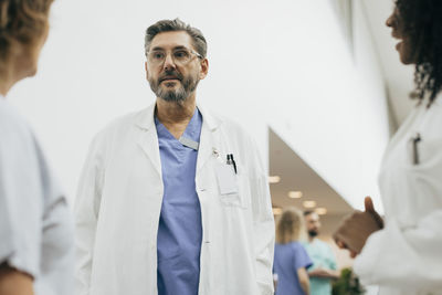 Mature male doctor wearing lab coat discussing with coworkers at hospital