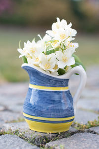 A beautiful mini bouquet of jasmine in a yellow-blue vase on a stone path