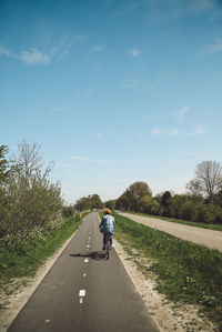 Rear view of woman riding bicycle on road against sky