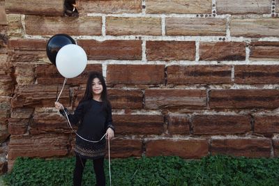 Portrait of a smiling young woman standing against brick wall