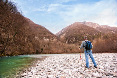 Rearview of male hiker standing by stream against mountains