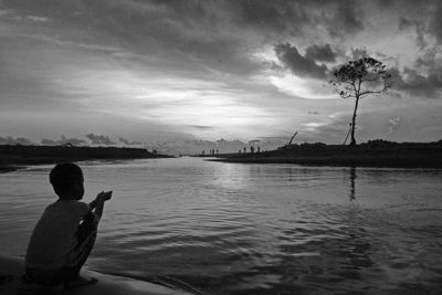 Rear view of man sitting on lake against sky