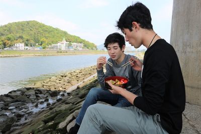 Teenage boys sitting at riverside with picnic