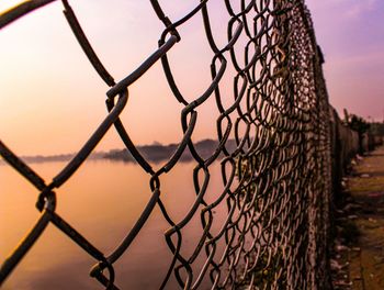 Close-up of chainlink fence against sky during sunset