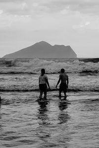 Rear view of men standing on beach against sky