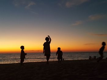 Silhouette children playing on beach against sky during sunset