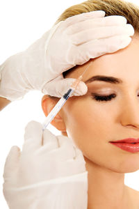 Cropped hands of beautician giving botulinum toxin injection to woman against white background