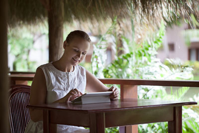 Smiling woman using digital tablet while sitting on chair at table