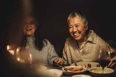 Happy senior woman laughing by female friend at dinner party