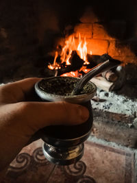 Close-up of hand holding container against fireplace