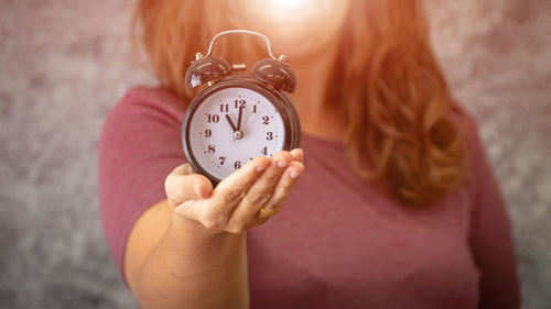 Close-up of woman hand holding clock against blurred background