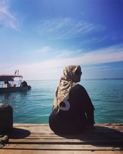 Rear view of woman sitting by sea against sky