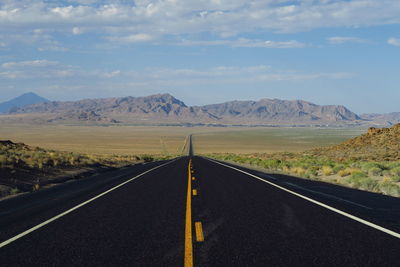 Empty road by mountains against sky