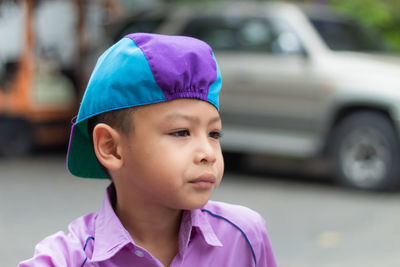 Cute boy looking away while standing against car on road