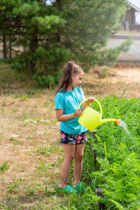 Little girl in a green t-shirt, watering a green bed of yellow watering can, in the garden