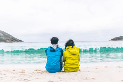Rear view of friends standing on beach against sky