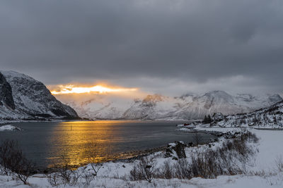 Scenic view of lake by snowcapped mountains against sky during sunset