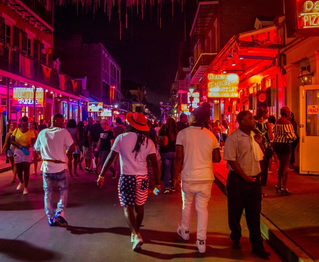 REAR VIEW OF PEOPLE WALKING ON ILLUMINATED STREET IN CITY AT NIGHT