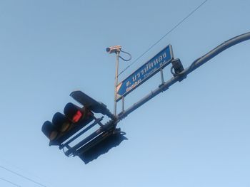 Low angle view of arrow sign and security camera against clear sky