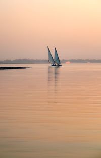 Sailboat sailing on sea against dramatic sky during sunset