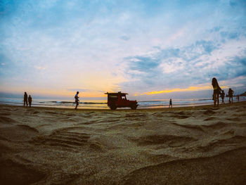 People at beach against sky during sunset