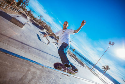 Man skateboarding against blue sky during sunny day