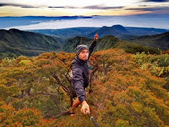 Portrait of man taking selfie while standing on tree over landscape against sky